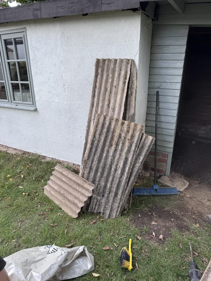 Corrugated roof sheets stacked beside an outbuilding before collection